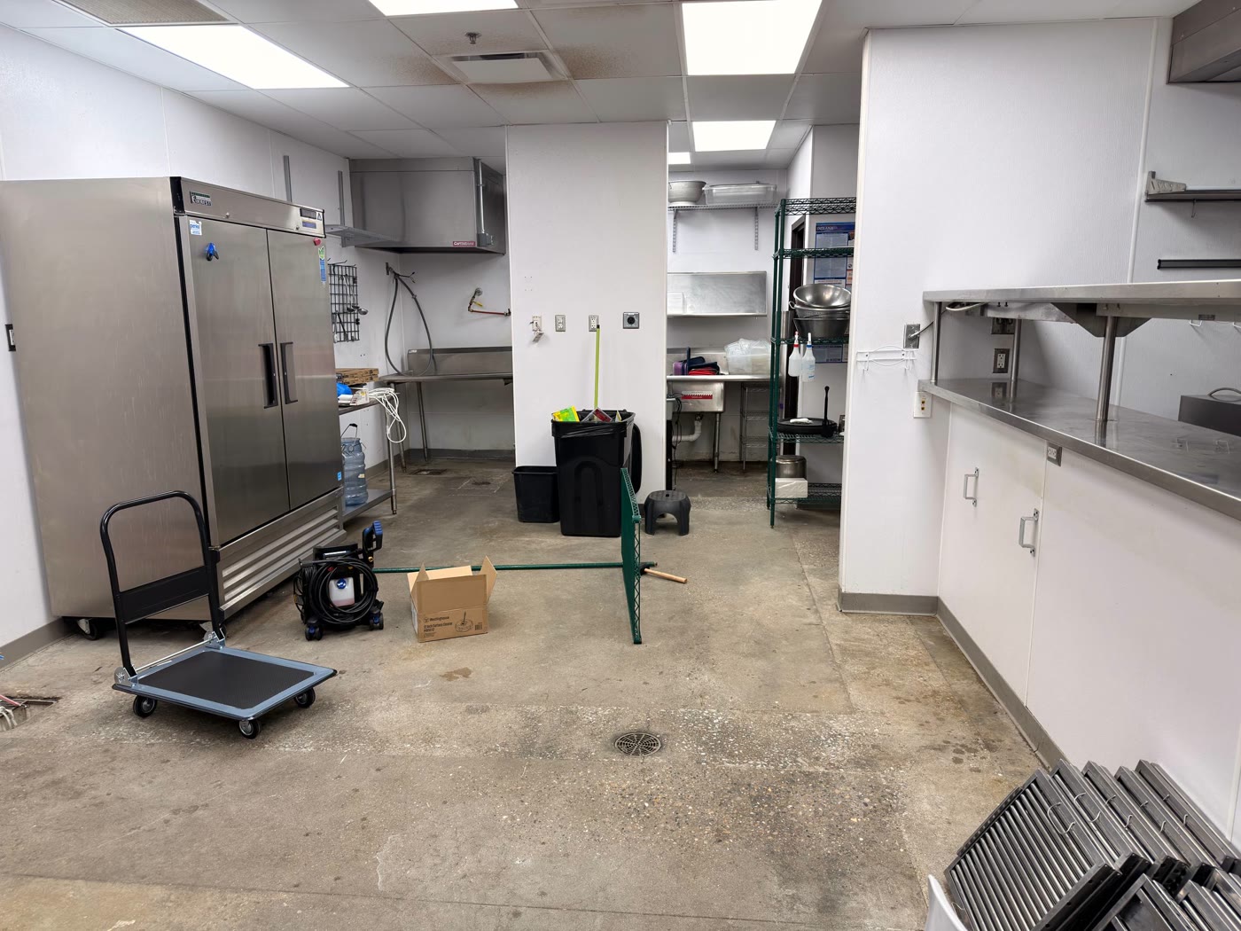 Kitchen area with commercial fridge, prep station, and exhaust hood staged for next phase